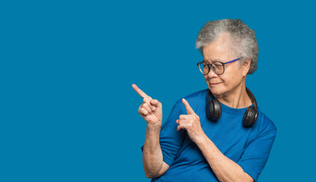 An elderly Asian woman with short gray hair pointing with two hands and fingers to the side with a...