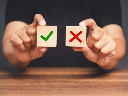 Yes or No. Hand holding two wooden cubes with a green checkmark and red cross. True and false symbols accept rejected for evaluation. Close-up photoの写真素材