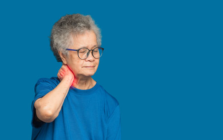 Senior woman suffering from neck pain standing over blue background. Space for text. Aged people and healthcare conceptの写真素材