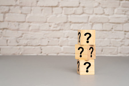 Question mark concept. Wooden cubes stacked with question mark symbols on a gray floor with white...