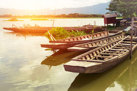 wooden boat float in reservoir with sunlight, mountain and clouds in vintage toneの写真素材