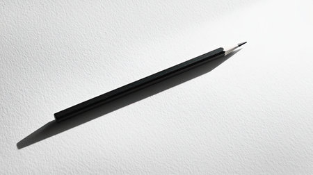 This image features a sleek black pencil casting a soft shadow on a bright white background. The minimalist scene captures creativity and simplicity, ideal for art or education themes.の素材