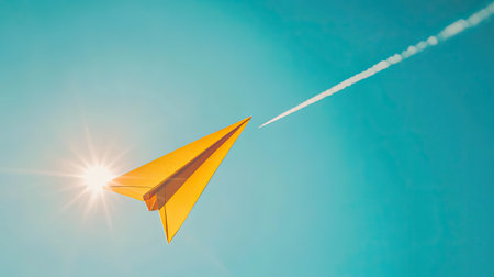 A vibrant yellow paper airplane flies high in a clear blue sky, embodying creativity and freedom, with a contrail gracefully tracing behind.の素材