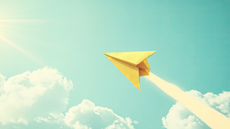 A vibrant yellow paper airplane glides through a clear blue sky, surrounded by soft clouds and bright sunlight, symbolizing creativity and inspiration.の素材