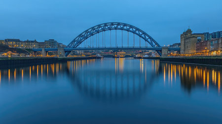 This captivating image showcases a serene evening view of a river reflecting the lights of a bridge and surrounding architecture in an urban setting.の素材