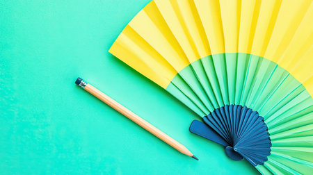 This image features a vibrant paper fan and a wooden pencil laid on a lively green background, perfect for creative projects. Ideal for design concepts.の素材