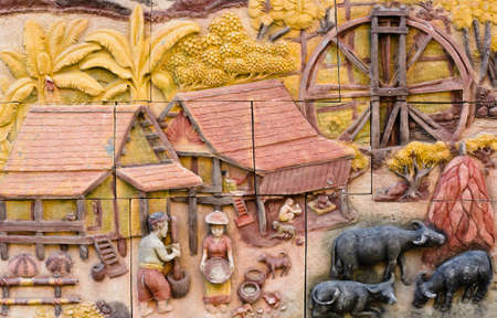 Stone carving of traditional Thai rural culture on temple wallの写真素材