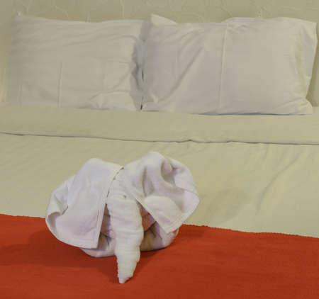 White towel in elephant shape on white bed in Thai style hotel bedroomの写真素材