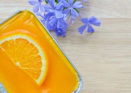 Orange soft cake with sliced orange fruit in aluminum foil tray on wooden backgroundの写真素材