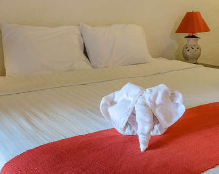 White towel in elephant shape on white bed in Thai style hotel bedroomの写真素材