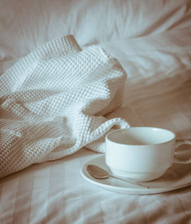 Empty coffee cup with white bathrobe on the bed. Vintage filter effect imageの写真素材