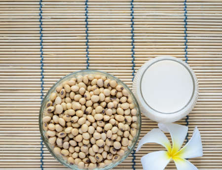 Fresh Soy milk (Soya milk) and dried soybean seeds on bamboo place mat with white plumeria flower. Traditional staple of East Asian cuisineの写真素材