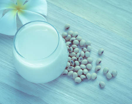 Fresh Soy milk (Soya milk) and dried soybean seeds on wooden background with white plumeria flower. Retro-Vintage filter effectの写真素材