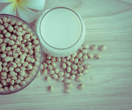 Fresh Soy milk (Soya milk) and dried soybean seeds on wooden background with white plumeria flower. Retro-Vintage filter effectの写真素材