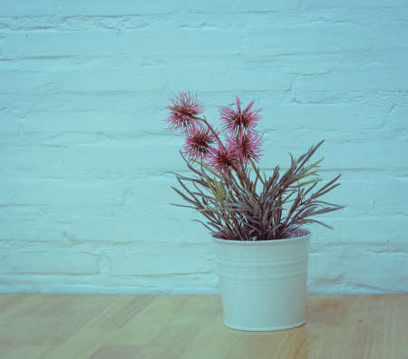 Decorated artificial flowers in flowerpot on wooden table with painted brick wall backgroundの写真素材