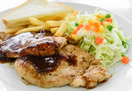 Grilled pork steak fillet with black pepper sauce, vegetable salad,  bread and french fries on white plateの写真素材