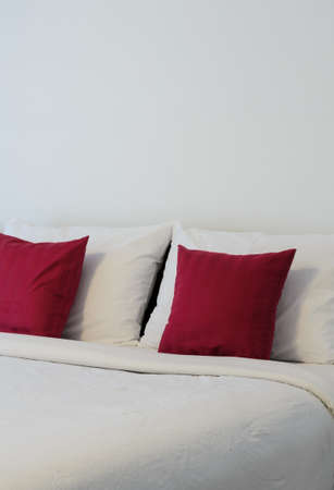 White bedroom with tidy bed and red pillowsの写真素材