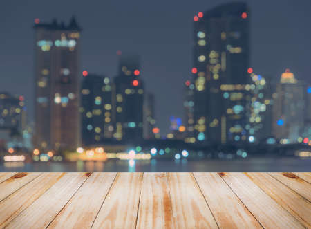 Empty wooden table top with blurred city skyline background  at night,  can be used for montage or...