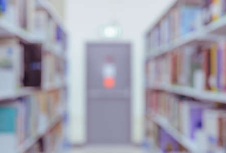 Blurred abstract background of bookshelves and interior of college or university library with textbooks and emergency exit. Vintage color image.の写真素材