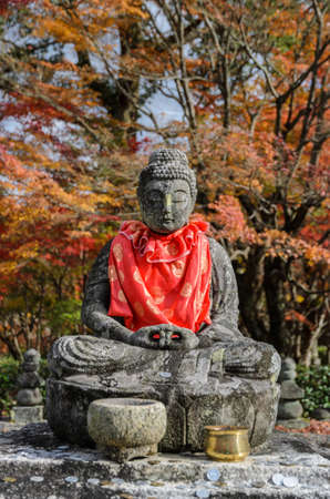 Stone statue of Buddha with autumn colored leaves in Adashino Nenbutsuji Temple, Kyoto, Japanのeditorial素材