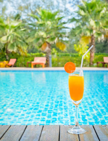 Orange juice with carrot slice in cocktail glass at outdoor swimming pool, summer tropical holiday conceptの写真素材