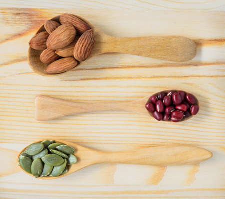 Dry ingredient of shelled almonds, adzuki red beans and pumpkin seeds in wooden spoon, top view on...