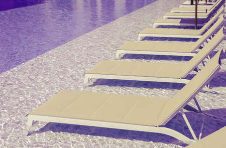 Swimming pool with clean water and sunbeds in purple and yellow tone color