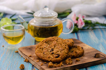 Homemade wholegrain cookies with raisin on wooden cutting board with tea and teapot on blue wooden tableの写真素材