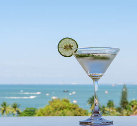 Fresh Lime soda  with lime slide in cocktail glass on wooden table with tropical sea view background. Refreshing drink in summer day for holiday concept.の写真素材