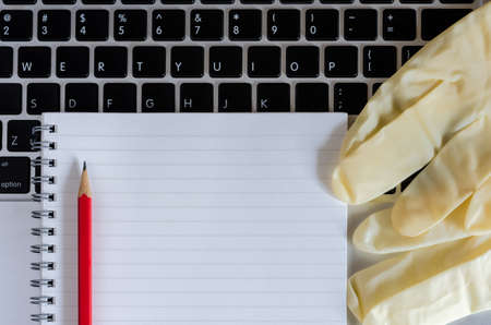 Spiral notebook, red pencil and medical gloves on laptop. Remote work and study.