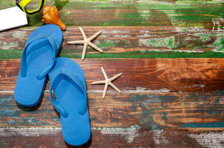 Flat lay summer beach accessories of blue flip flops , smartphone, snorkel with seashell and starfish on wooden background. Summer vacation and travel concept.の写真素材