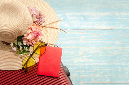 Top view traveller accessories of red luggage, passport, sunglasses and straw flowered hat on light blue wooden background. Summer holiday and travel concept.の写真素材