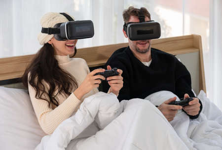 Happy couple wearing Virtual reality headset and having fun while playing VR games together in bed....