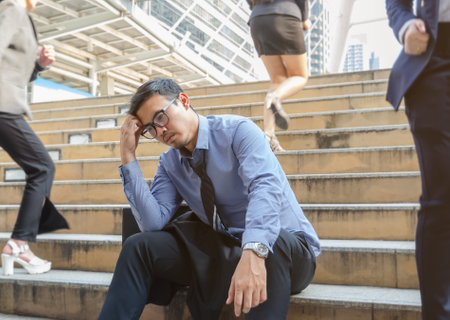 Depressed business man sitting still on busy stairs outdoors with blurry businesswomen walking past him in the city.の写真素材