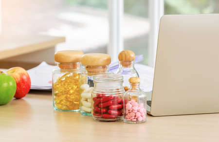 Pharmaceutical medicine and capsules with fruits and laptop computer on nutritionist doctor desk in...