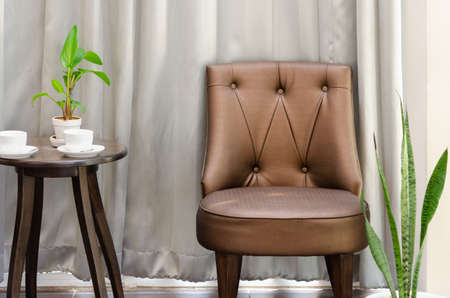 Living room or lobby interior with brown chair and round side table with coffee cup and green plantの写真素材