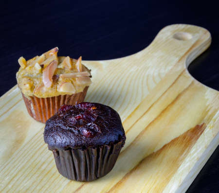 Chocolate cherry muffin and banana cupcake with almond toping on wooden boardの写真素材