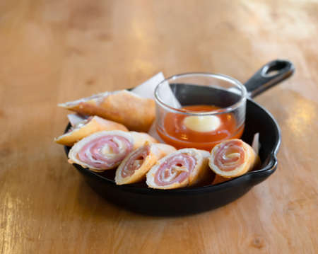 Fried ham and cheese spring rolls served with hot chilli sauce on black panの写真素材