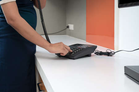 Maid in blue uniform using telephone at hotel roomの写真素材