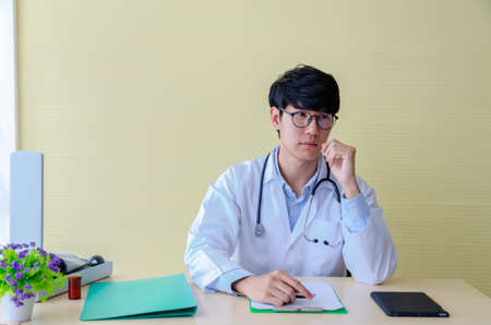 Portrait of male doctor wearing lab coat and looking seriously while sitting at desk in hospital office. Healthcare concept.の写真素材