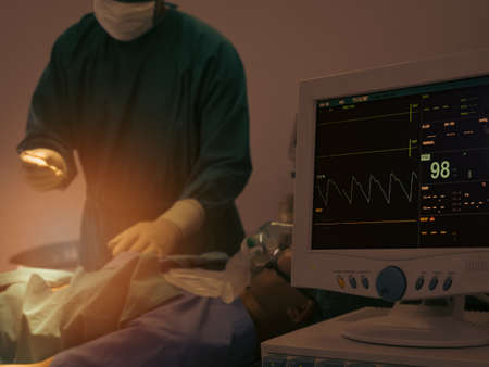 Monitoring of Electrocardiogram and saturation O2  of patient in hospital operating room with blur surgery in backgroundの写真素材