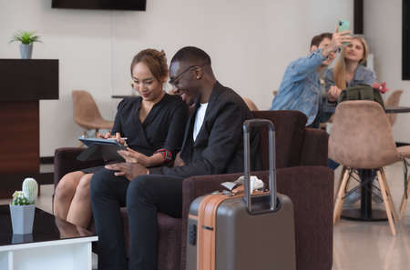 Two happiness business travellers discussing presentation or new ideas for business project with tablet PC while waiting for flight in airport loungeの写真素材