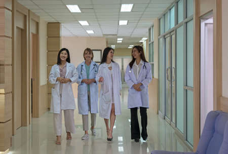 One mature doctor and three young  females doctor walking and discussing diagnosis in hospital corridor. Teamwork and healthcare conceptの写真素材