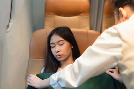 Stewardess taking care of passenger. Flight attendant covering tired sleepy woman with blanket during trip. Flight with comfort conceptの写真素材