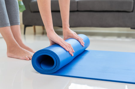 Cropped image of woman rolling blue mat after doing yoga exercise workout in living room at home. Healthy life and fitness training workout conceptの写真素材
