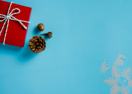 Christmas background of red gifts box with white and silver cord rope ribbon, conifer cones, and acorn on blue paper background. Flat layout with copy space design.の写真素材
