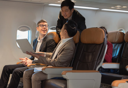 Businessman passengers having discussion, working together on laptop in airplane cabin. Business work and travel conceptの写真素材