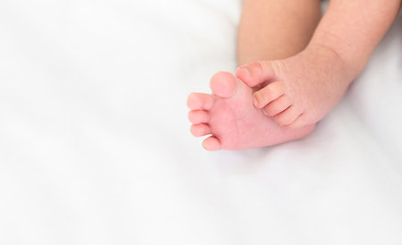 Cute little newborn baby feet on white bedding at home, soft focus background with copy space.