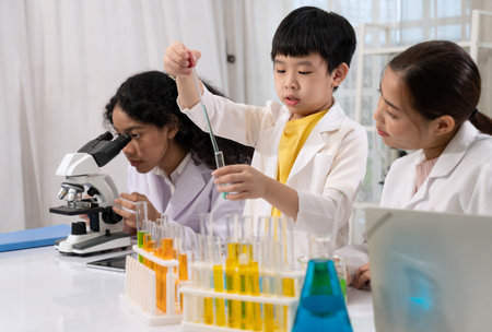Pupil wearing white laboratory coat and learning science experiment by using eye dropper for dropping blue liquid to test tube in science laboratory room with scientist teacher. Children education concept with experiment, fun and enjoy class.の写真素材