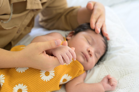 Hand of mother holding finger of newborn hand. Adorable newborn baby sleeping on bed at home while mom lying down nursing baby girl and gently touching on head with love. Care, love and protection concept.の写真素材